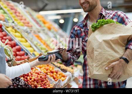 Den mittleren Abschnitt Portrait von lächelnden jungen Mann bezahlen per Smartphone bei Farmers Market, Kopie Raum Stockfoto