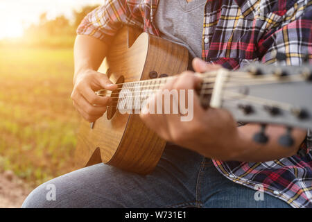 Asiatischer Mann Gitarre zu spielen, die grüne Reisfelder in den Sonnenuntergang. Auf dem Land von Thailand Stockfoto