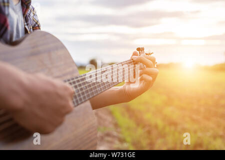 Asiatischer Mann Gitarre zu spielen, die grüne Reisfelder in den Sonnenuntergang. Auf dem Land von Thailand Stockfoto