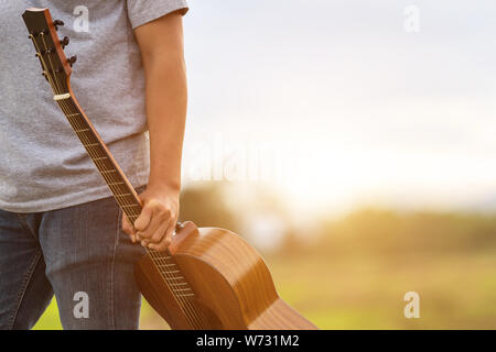 Asiatischer Mann Gitarre zu spielen, die grüne Reisfelder in den Sonnenuntergang. Auf dem Land von Thailand Stockfoto