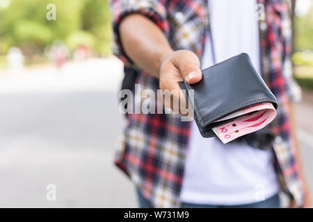 Hand von asiatischen Touristen geben Banknoten- und schwarzen Mappe, die er in Die touristische Attraktion gefunden. Wallet Konzept zu verlieren. Stockfoto