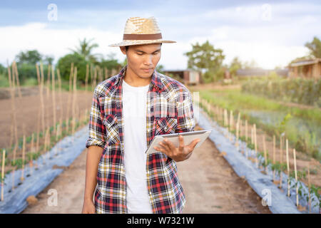 Portrait von jungen asiatischen smart Bauer Holding Tablet in seiner biologischen Bauernhof. Technik und Landwirtschaft Konzept Stockfoto