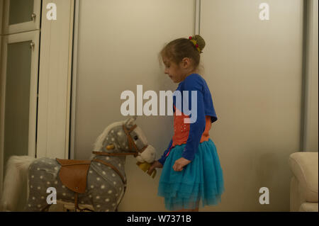 Kleines Mädchen spielt mit einem Pferd Gurney. Das Kind sitzt auf einem Pferd. Schöne Mädchen ist glücklich sitzen auf einem Spielzeug Pferd. Einen blauen Rock, eine orange Stockfoto