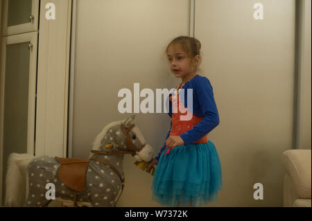 Kleines Mädchen spielt mit einem Pferd Gurney. Das Kind sitzt auf einem Pferd. Schöne Mädchen ist glücklich sitzen auf einem Spielzeug Pferd. Einen blauen Rock, eine orange Stockfoto