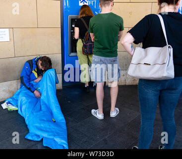 Obdachloser sitzt der öffentlichen mit ATM Cash Dispensing Machine auf der Royal Mile in Edinburgh, Schottland, VEREINIGTEN KÖNIGREICH an Warteschlange Stockfoto
