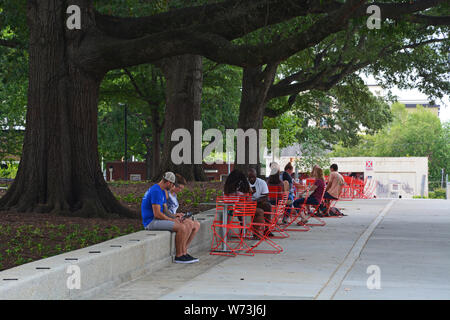 Besucher sitzen im Schatten der hundertjährigen Bäume im revitalisierten Moore Square (2019) in der Innenstadt von Raleigh, North Carolina. Stockfoto