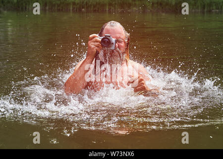 Reife bärtige weiße Mann Schwimmen im Fluss ist und Fotos mit wasserdichte Kamera, eco - Tourismus. Stockfoto