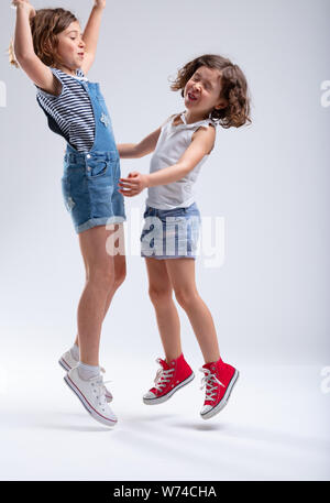 Zwei junge Schwestern springen und gemeinsam lachen in Blue Denim Shorts, wie Sie Ihren Sommer Urlaub auf einem weißen Hintergrund genießen Stockfoto