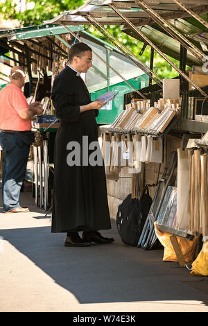 Paris, Frankreich, 04. Juli 2017: ein Priester in der soutane Kleidungsstück blicke auf ein Buch von einem Der bookstalls entlang der Seine Bürgersteig. Stockfoto