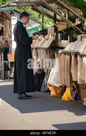 Paris, Frankreich, 04. Juli 2017: ein Priester in der soutane Kleidungsstück blicke auf ein Buch von einem Der bookstalls entlang der Seine Bürgersteig. Stockfoto