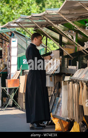 Paris, Frankreich, 04. Juli 2017: ein Priester in der soutane Kleidungsstück blicke auf ein Buch von einem Der bookstalls entlang der Seine Bürgersteig. Stockfoto