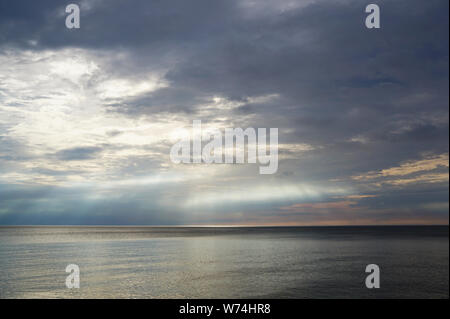 Sonnenuntergang über dem Meer, wo die Sonnenstrahlen über der Wasseroberfläche glänzen. Weit entfernt am Horizont, das helle Sonnenlicht ist sichtbar auf dem dunklen Wasser. Stockfoto