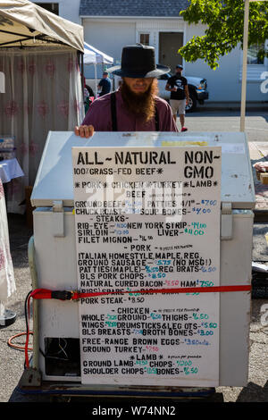 Ein Amish Anbieter hinter einem Gefrierschrank mit einem Schild mit Werbung Nicht-GVO-Fleisch und Eier auf dem Wochenmarkt in der Innenstadt von Fort Wayne, Indiana, USA. Stockfoto