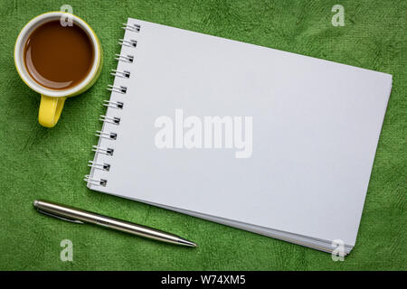 Leere Spirale Art Skizzenbuch gegen grüne strukturierte Rinde Papier mit einer Tasse Kaffee Stockfoto