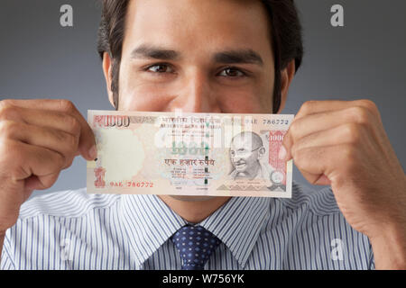 Indischer Geschäftsmann eine Banknote über den Mund halten Stockfoto