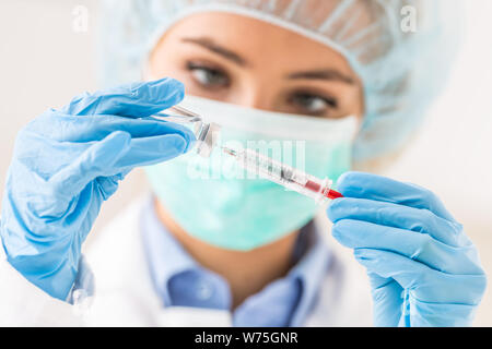 Ärztin arbeiten mit Nadel und ampulle von Medizin. Ein Wissenschaftler in sterilen Kleidung ist ein Impfstoff, der Droge. Stockfoto