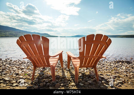 Zwei Stühle aus Holz am Ufer eines Sees mit Blick auf das Wasser. Stockfoto