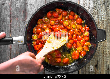 Person kochen Gericht mit gebratenen Tomaten, Sauce für Pasta, gesundes Essen, italienisches Essen vorbereiten, detaillierte Ansicht von Händen und Pan, Overhead Stockfoto