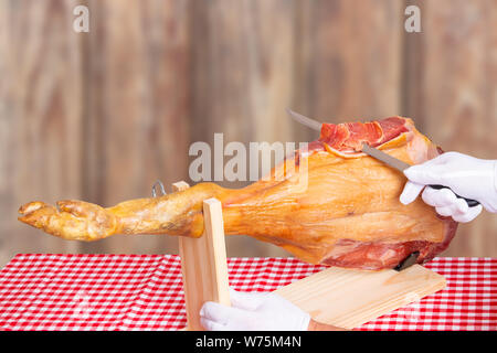 Schinken oder Jamón Serrano. Professionelle Cutter schneiden Stücke aus einem ganzen Schenkel eines Serrano Schinken vor verschwommen im Landhausstil Hintergrund. Spanis Stockfoto