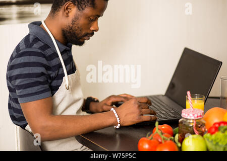 Portrait von schweren afrikanischen amerikanischen Jungen bärtigen Mann Arbeiten am Laptop, mit Handy und trinken Orangensaft in der Küche am Morgen. Stockfoto