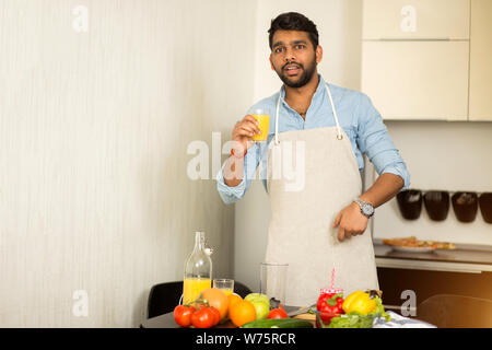 Hübscher junger angenehme bärtigen Inder trinken frisch gepressten O-Saft, Gemüse Smoothie, Zubereitung von Salat in der Küche. Gesunde f Stockfoto
