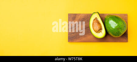 Organische Avocados halbieren mit Saatgut und ganze Früchte auf Holz- Fach auf gelb Tabelle Hintergrund. gesund Super Foods für Ernährung. Frisches Gemüse vom Bauernhof. k Stockfoto