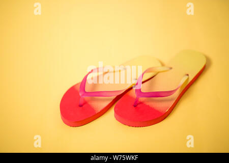 Ein studio Foto von rosa Koralle gelb Sandalen. Bunte Flip-flops auf gelbem Hintergrund. Ansicht von oben, Nahaufnahme. Stockfoto