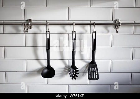 Kunststoff schwarz Küchenutensil hängen am weißen Stein Wand. Foto von Kochgeschirr. Küchengeräte hängenden weißen Stein Hintergrund. Stockfoto