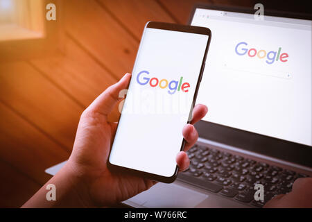 Bangkok, Thailand - August 5, 2019: Frau Hände halten Smartphone mit Google Logo auf dem Bildschirm und Google Chrome Webbrowser anzeigen auf dem Laptop. Stockfoto