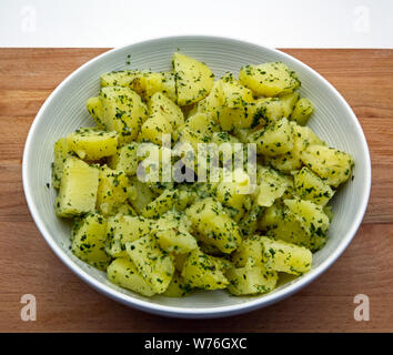 Gekochte Kartoffeln mit Petersilie in Weiß Schüssel, hölzernen Tisch Stockfoto