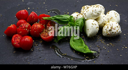 Mozzarella und Tomaten auf schwarzem Schiefer. Öl, origan und Petersilie Stockfoto