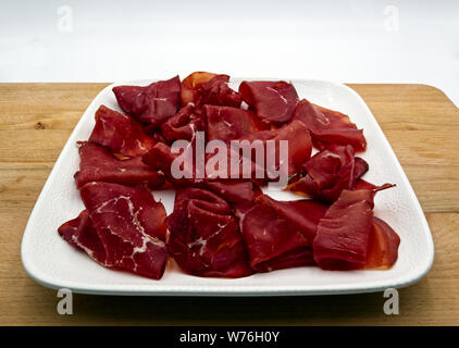 Scheiben der italienischen Bresaola auf weiße Platte. Holztisch, weißer Hintergrund Stockfoto