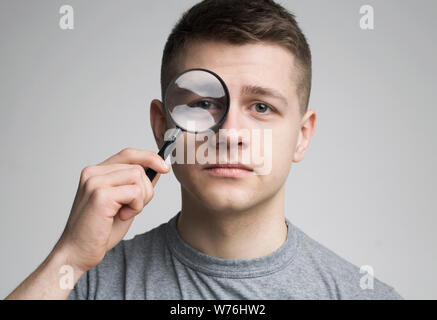 Junger Mann mit Lupe in der Nähe von Eye Stockfoto