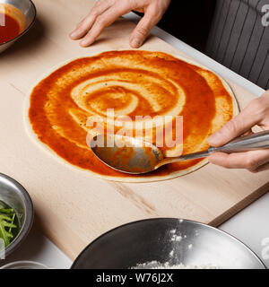 Mann hinzufügen Tomatensauce auf Pizza, Nahaufnahme Stockfoto