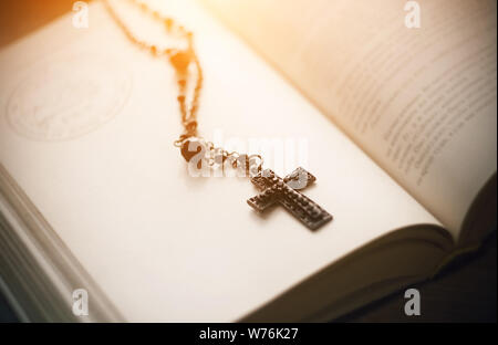 Den heiligen schwarzen Gothic Kreuz auf eine Kette mit schwarzen Perlen liegt auf den Seiten eines offenen Buches, in der die Texte und die Umrisse des Pentagramms, Illu Stockfoto