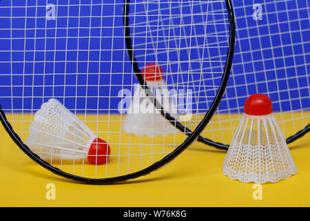 Badminton. Drei Bälle und zwei Badminton Schläger. Die farbigen Hintergrund ist blau und gelb. Idee für ein Magazin. Stockfoto