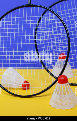 Badminton. Drei Bälle und zwei Badminton Schläger. Die farbigen Hintergrund ist blau und gelb. Idee für ein Magazin. Stockfoto