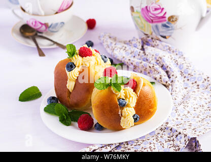 Rum baba dekoriert mit Schlagsahne und frischen Himbeeren, Heidelbeeren. Savarin mit Rum, Sahne und Beeren. Italienische Küche Stockfoto