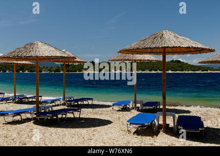 Stroh Sonnenschirme und Liegestühle am Strand auf der griechischen Insel Meganisi Stockfoto