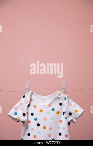 Cute Polka Dot Baby Body Anzug hängen von einer Linie gegen einen rosa Hintergrund Stockfoto