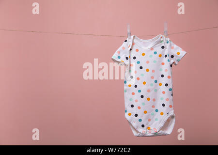 Cute Polka Dot Baby Body Anzug hängen von einer Linie gegen einen rosa Hintergrund Stockfoto