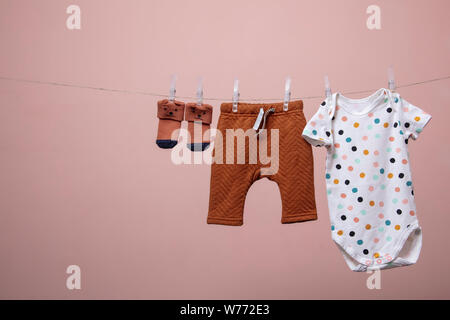 Cute Baby Outfit hängen von einer Linie gegen einen rosa Hintergrund Stockfoto