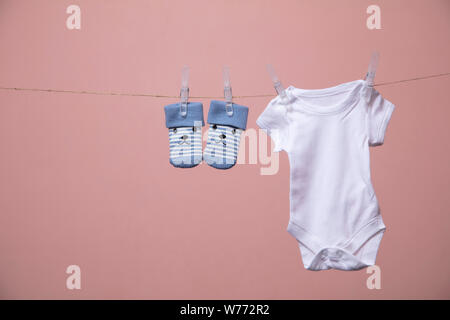 Weißer Baby Body Anzug hängen von einer Linie gegen einen rosa Hintergrund Stockfoto