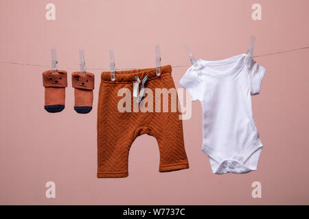 Cute Baby Outfit hängen von einer Linie gegen einen rosa Hintergrund Stockfoto