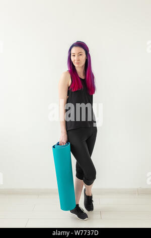 Schlanke junge Mixed Race girl Hipster mit gefärbten Haaren falten Gymnastik Matte nach Yoga im Fitnessstudio. Gesunder Lebensstil und Fitness Concept Stockfoto