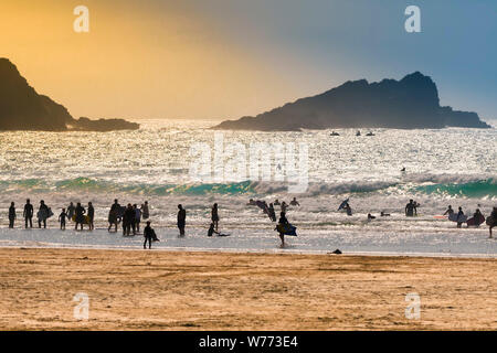 Urlauber silhouetted gegen die untergehende Sonne auf den Fistral Beach in Newquay in Cornwall. Stockfoto