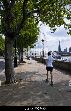 Ein Jogger läuft neben der Themse in London, Großbritannien, mit dem Shard Skyscraper auf die Skyline zu sehen. Stockfoto