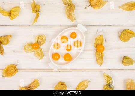 Viele viele Stücke von frischem Orange Physalis in weiße, ovale Keramik Schüssel flatlay auf weißem Holz Stockfoto