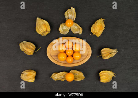 Menge ganze Frische orange Physalis in Mandala am Oval Bambus Untersetzer flatlay arrangiert auf grauem Stein Stockfoto