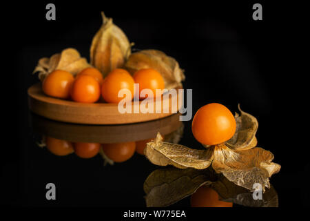 Menge ganze Frische orange Physalis auf runden Bambus Untersetzer auf schwarzem Glas isoliert Stockfoto